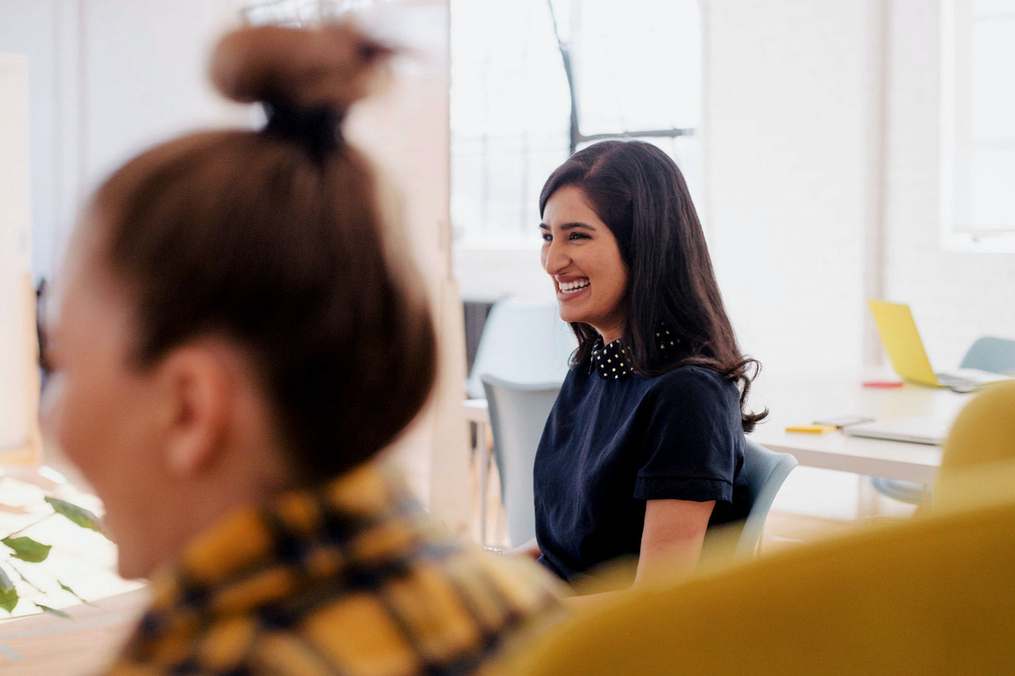 Two people sitting in a room in chairs smiling